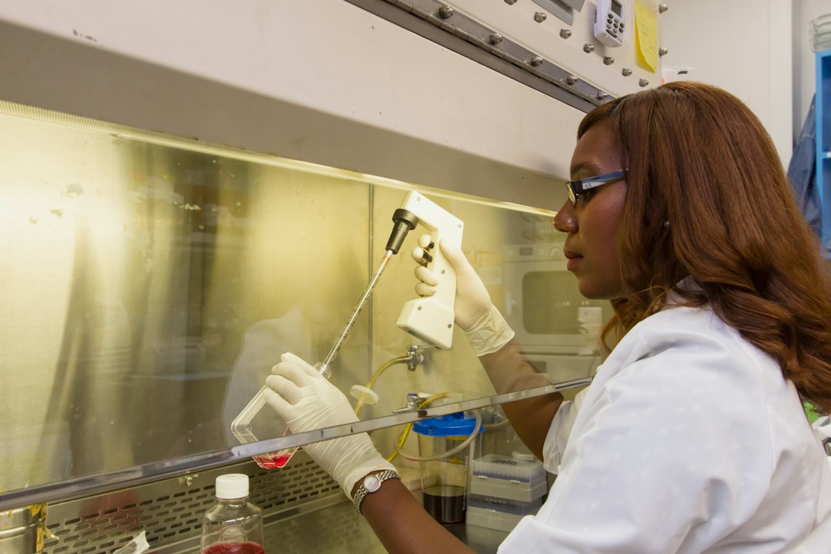 a woman in white lab coat and gloves working on a machine